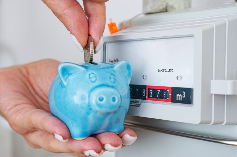 Hand inserting money into piggy bank in front of gas meter